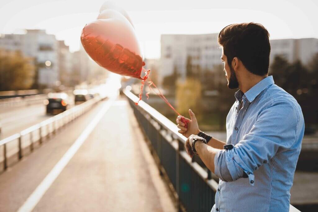 hombre que sostiene un globo de corazón rojo cerca de la carretera